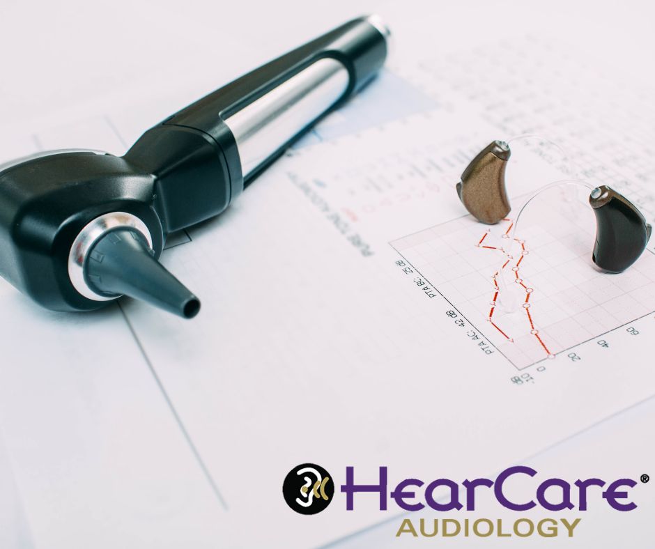 An otoscope and a pair of brown and black hearing aids on top of a paper with a graph printed on it